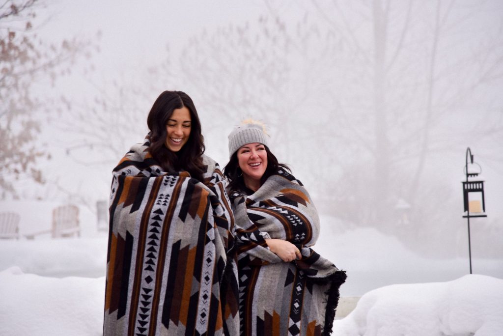 two spa goers enjoying their time at the spa in a snowy setting while wearing a mini tipi blanket