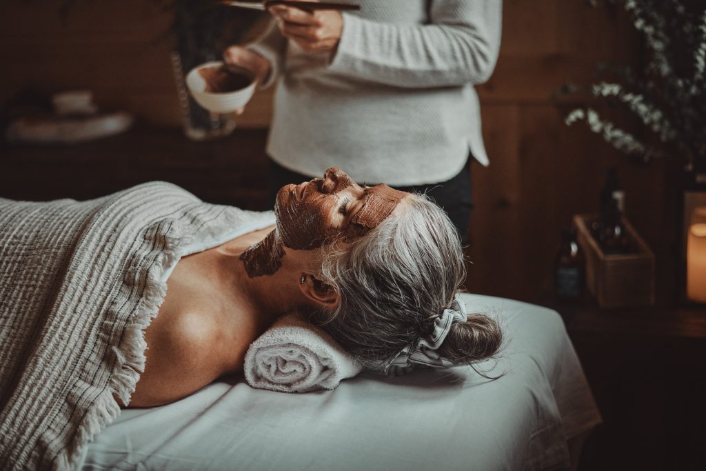 A woman is lying comfortably, her face adorned with a Lumëa Speciality facial treatment. The soft, ambient lighting gently illuminates the room, creating a tranquil atmosphere. 