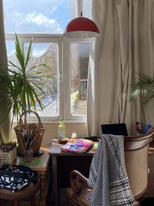 desk by a window with plants, blankets and books